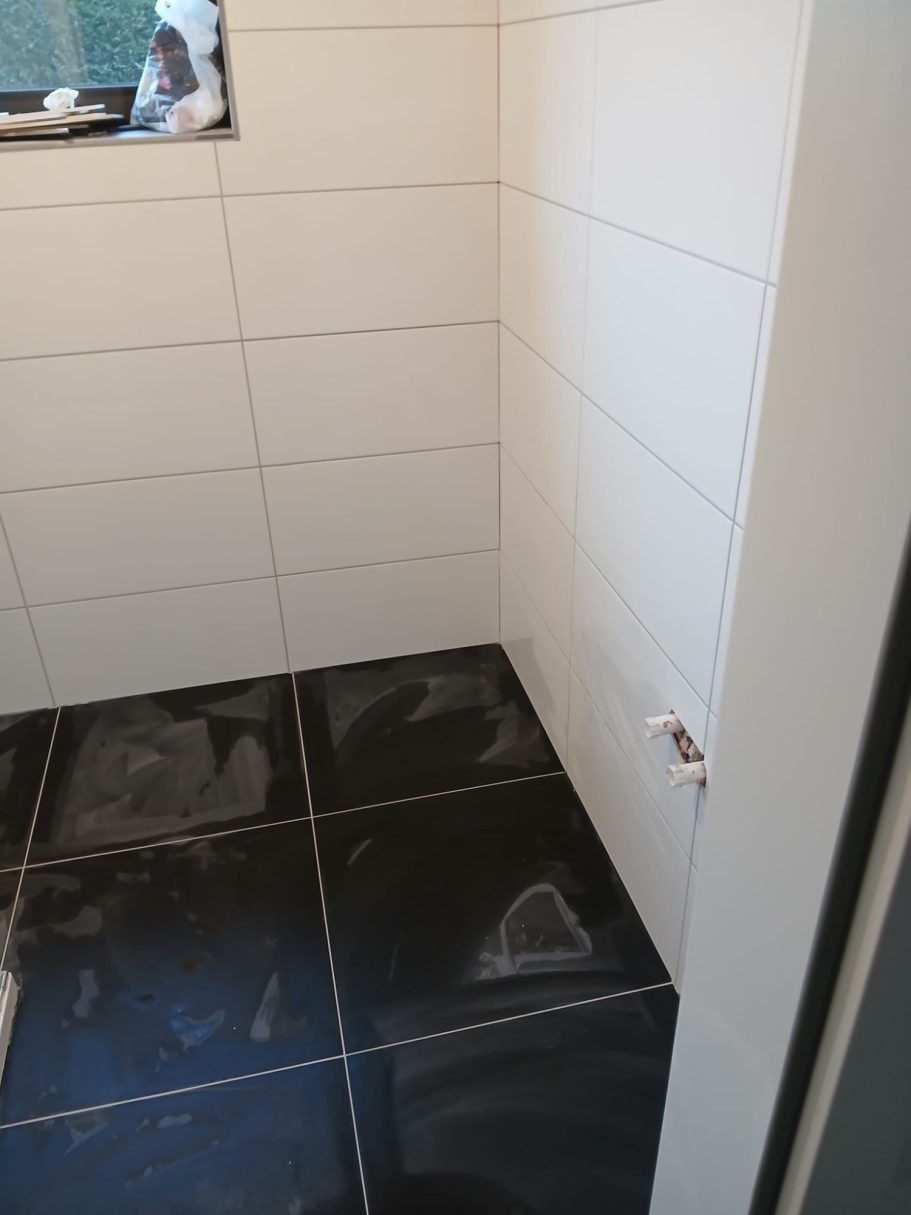 Eckbereich mit weißen Wandfliesen und schwarzen Bodenfliesen.