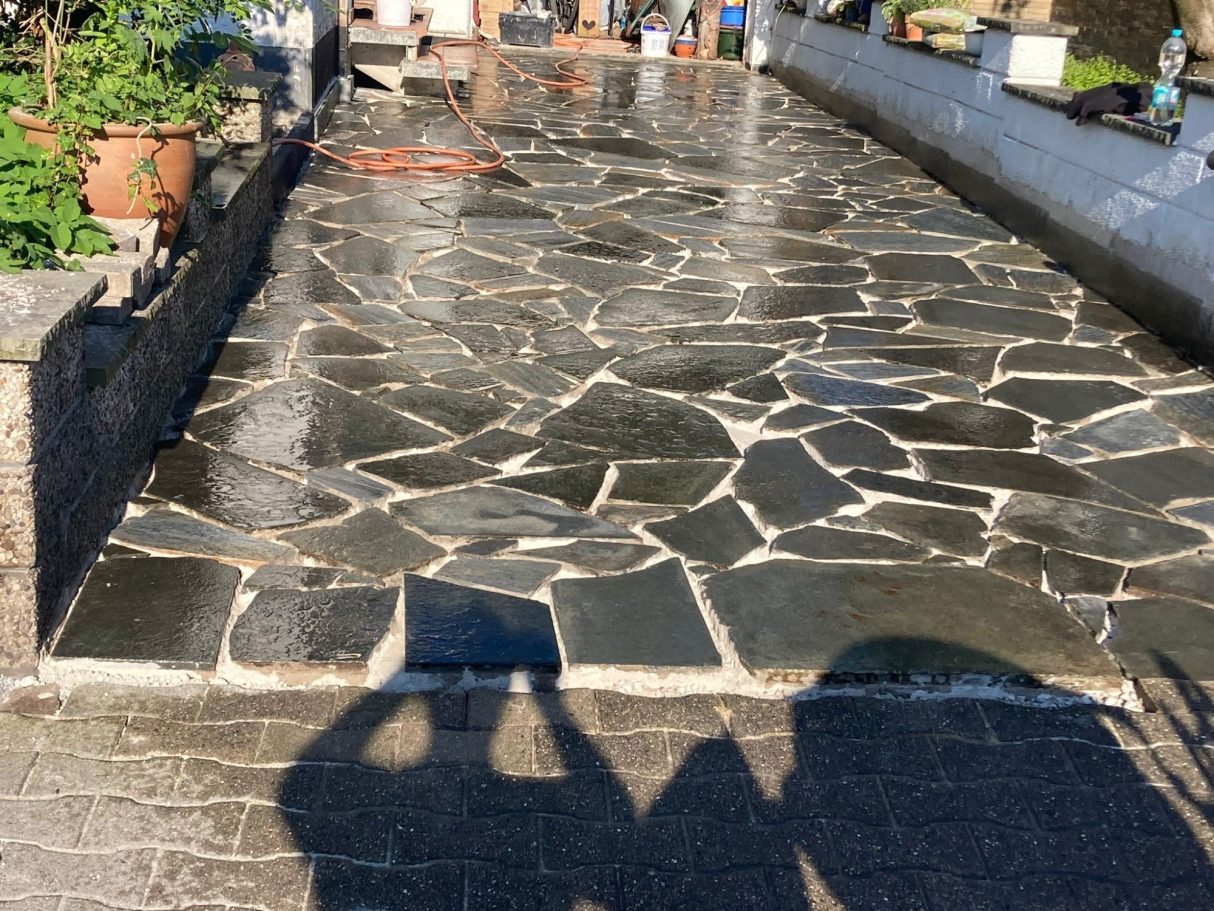 Fleckige Steinplatte mit nassen Flächen in einer sonnigen Umgebung.